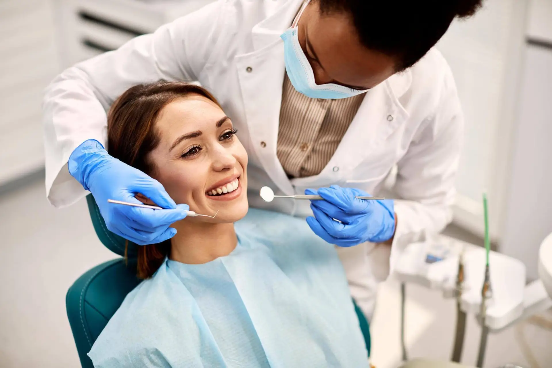 Dentist performing checkup on smiling female patient.