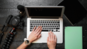 Person typing on a laptop with camera nearby.