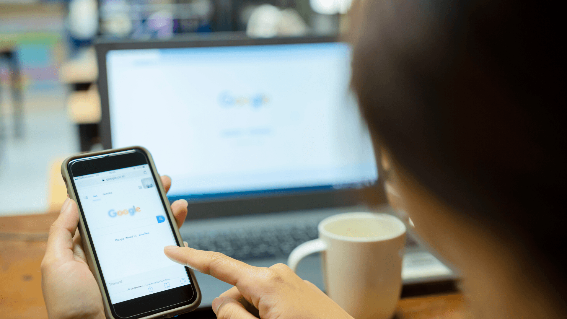 Person using smartphone and laptop with Google search.